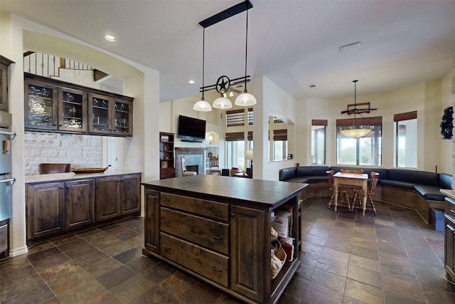 7576 River Ridge Drive, College Station, TX 77845 - kitchen with stone tile flooring, dark brown cabinetry, a fireplace, dark countertops, and open floor plan