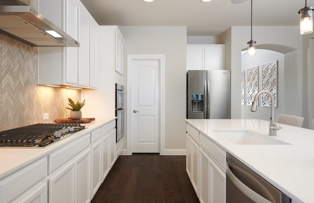 kitchen featuring wall chimney range hood, a sink, dark wood finished floors, backsplash, and stainless steel appliances