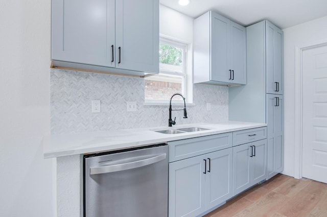 kitchen with light stone countertops, a sink, light wood-type flooring, tasteful backsplash, and stainless steel dishwasher