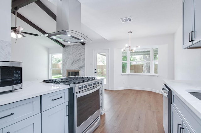 kitchen featuring visible vents, island range hood, light wood finished floors, appliances with stainless steel finishes, and hanging light fixtures