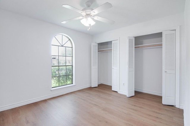 unfurnished bedroom with multiple closets, baseboards, light wood finished floors, and ceiling fan