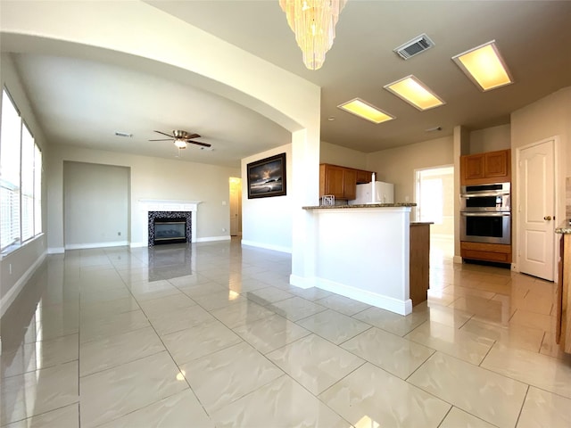 kitchen featuring double oven, visible vents, brown cabinetry, and ceiling fan with notable chandelier