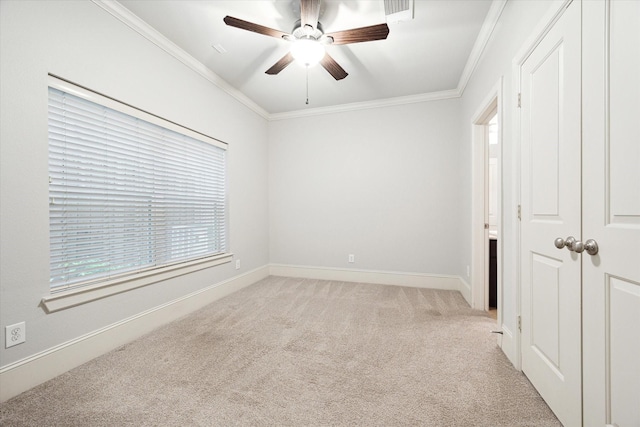 spare room featuring light carpet, a ceiling fan, baseboards, visible vents, and ornamental molding