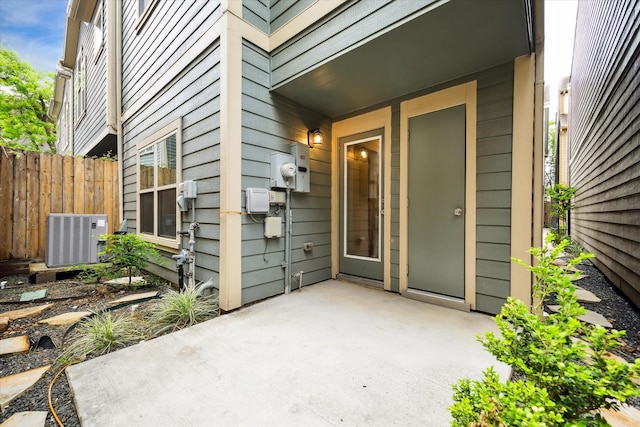 view of exterior entry featuring a patio area, central AC, and fence