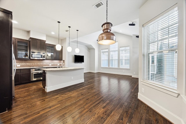 kitchen featuring dark wood-style flooring, dark brown cabinetry, glass insert cabinets, tasteful backsplash, and appliances with stainless steel finishes