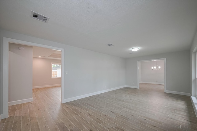 unfurnished room with baseboards, a notable chandelier, light wood-style flooring, and visible vents