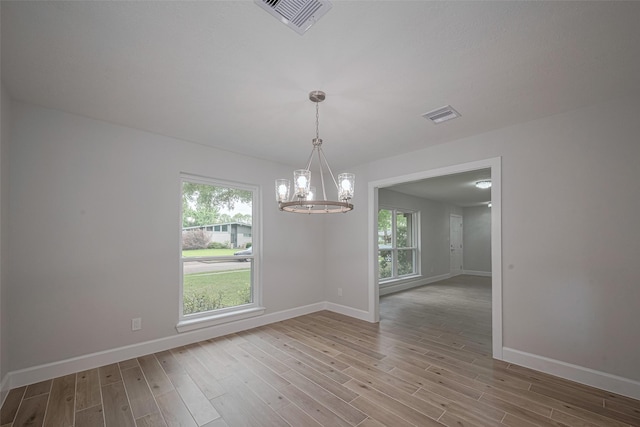 spare room with a notable chandelier, visible vents, baseboards, and wood finished floors