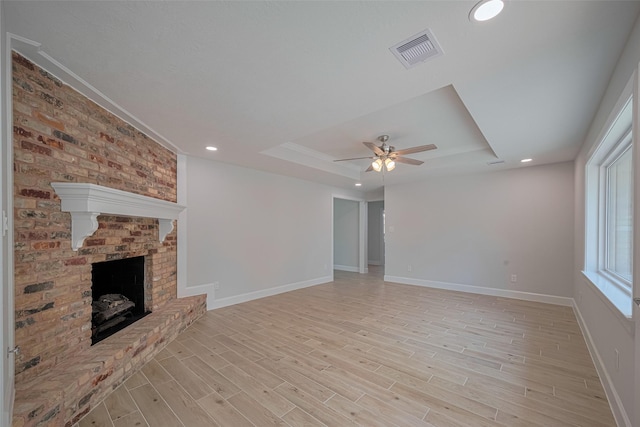 unfurnished living room featuring a raised ceiling, a fireplace, a ceiling fan, baseboards, and visible vents