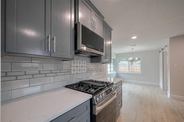 kitchen featuring baseboards, decorative backsplash, light wood finished floors, and appliances with stainless steel finishes
