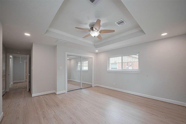unfurnished bedroom with visible vents, crown molding, baseboards, a tray ceiling, and light wood-style flooring
