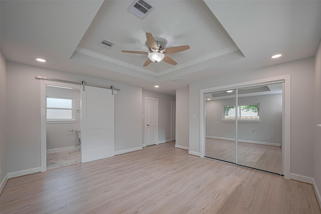 unfurnished bedroom featuring light wood-style floors, a tray ceiling, a barn door, and visible vents