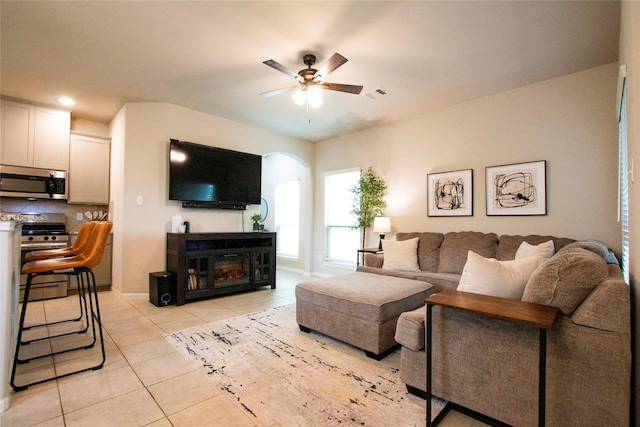 living room with light tile patterned flooring, ceiling fan, a fireplace, arched walkways, and visible vents