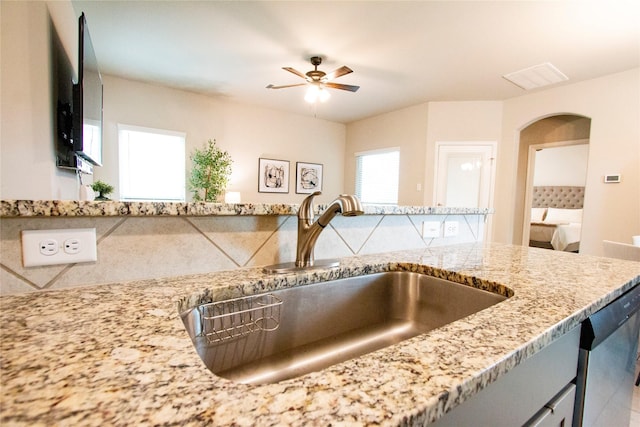 details featuring light stone counters, a sink, arched walkways, a ceiling fan, and visible vents