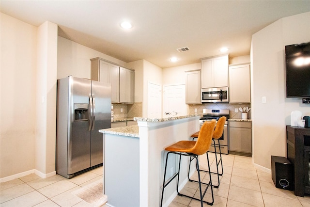 kitchen featuring a kitchen island, a breakfast bar area, tasteful backsplash, appliances with stainless steel finishes, and light tile patterned floors