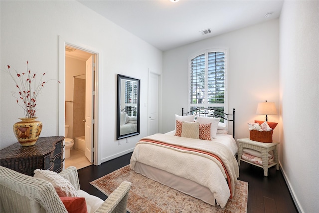bedroom with connected bathroom, baseboards, visible vents, and wood finished floors