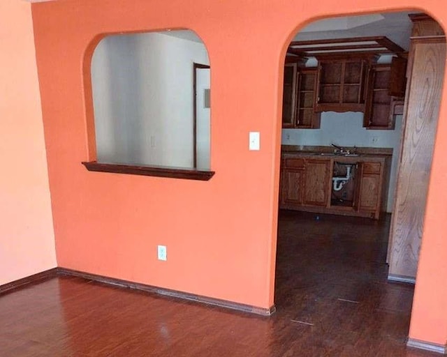 unfurnished room featuring a sink, baseboards, dark wood finished floors, and arched walkways