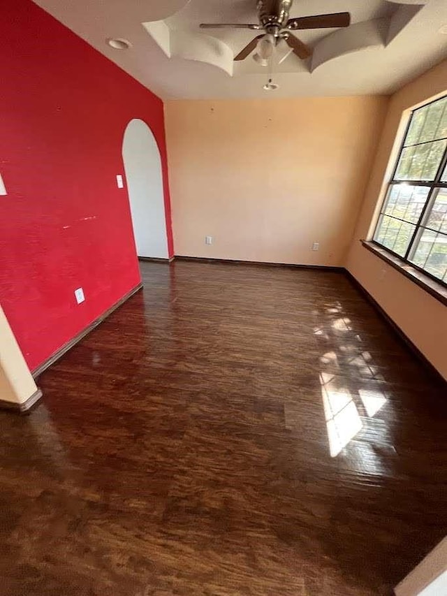 spare room featuring a ceiling fan, baseboards, wood finished floors, and arched walkways