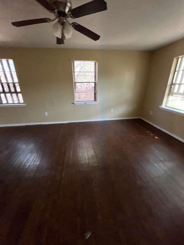 empty room with baseboards, a ceiling fan, and dark wood finished floors