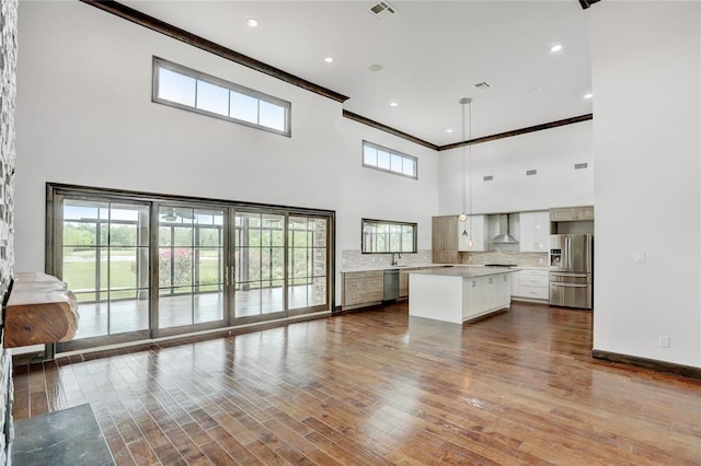 unfurnished living room featuring dark wood-style flooring, a high ceiling, visible vents, and ornamental molding