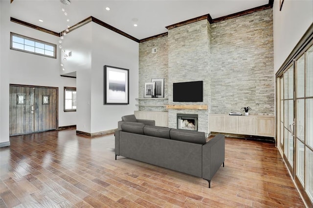 living room featuring crown molding, wood finished floors, a stone fireplace, baseboards, and a high ceiling