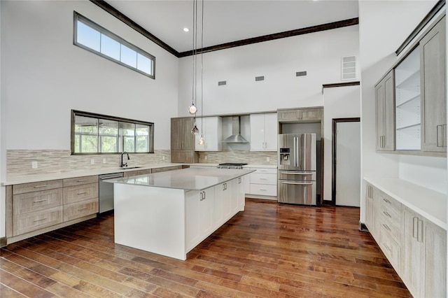 kitchen featuring wall chimney range hood, appliances with stainless steel finishes, a towering ceiling, visible vents, and ornamental molding