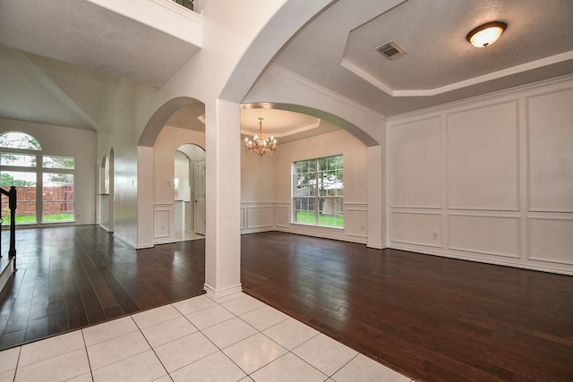 interior space with a tray ceiling, wood-type flooring, a decorative wall, and a chandelier