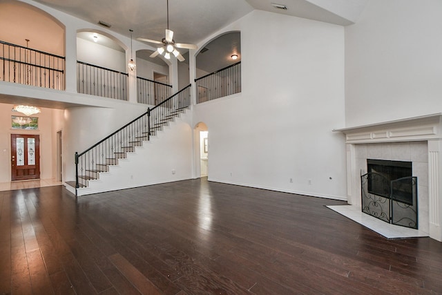 unfurnished living room featuring a high ceiling, wood-type flooring, arched walkways, a ceiling fan, and a tile fireplace