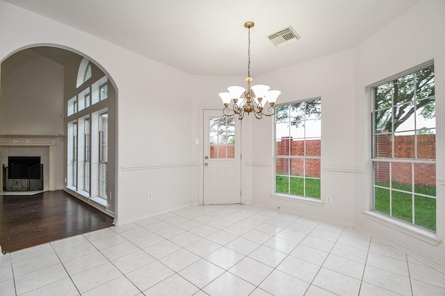 unfurnished dining area with visible vents, a tiled fireplace, a wealth of natural light, and an inviting chandelier