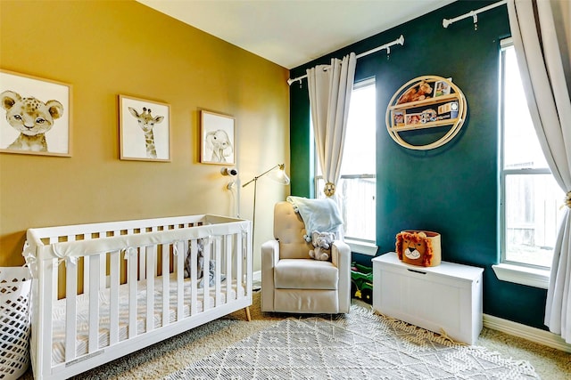 bedroom featuring a nursery area, baseboards, and carpet flooring