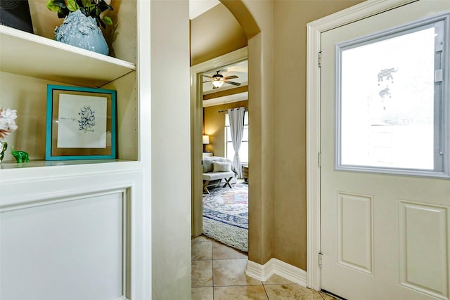doorway with arched walkways, baseboards, ceiling fan, and light tile patterned flooring