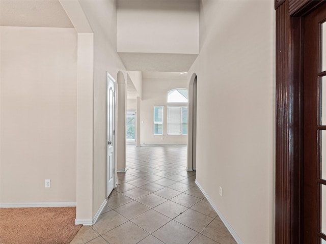corridor with light tile patterned floors, arched walkways, and baseboards