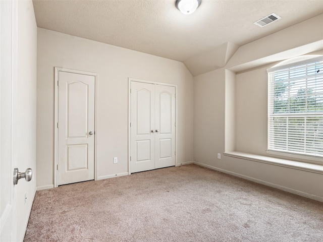 unfurnished bedroom with visible vents, carpet flooring, baseboards, and lofted ceiling