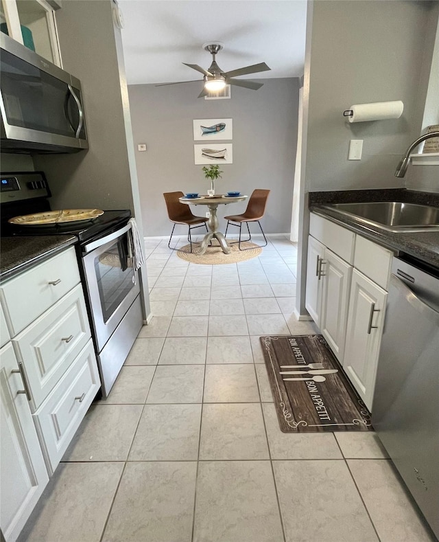 kitchen featuring dark countertops, a sink, white cabinets, stainless steel appliances, and light tile patterned flooring