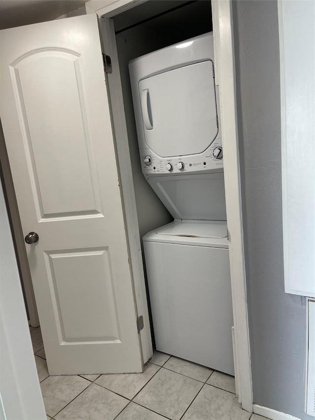clothes washing area featuring laundry area, light tile patterned flooring, and stacked washer / dryer