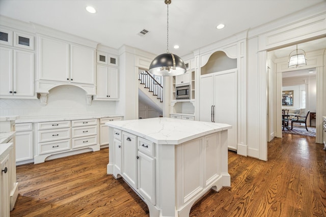 kitchen featuring white cabinets, stainless steel microwave, visible vents, and a kitchen island