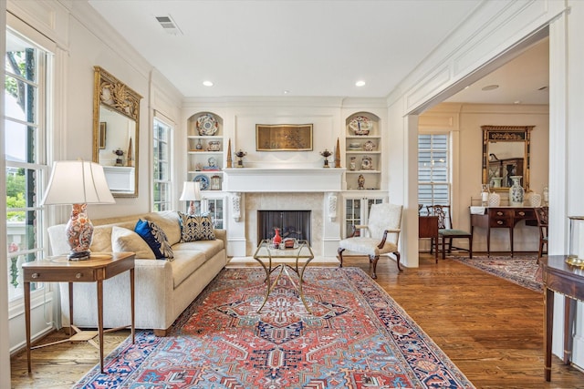 living room featuring built in shelves, ornamental molding, wood finished floors, and visible vents