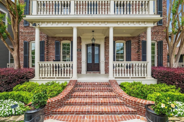 view of exterior entry with covered porch, brick siding, and a balcony