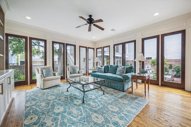 living room with light wood-type flooring, crown molding, ceiling fan, and a decorative wall