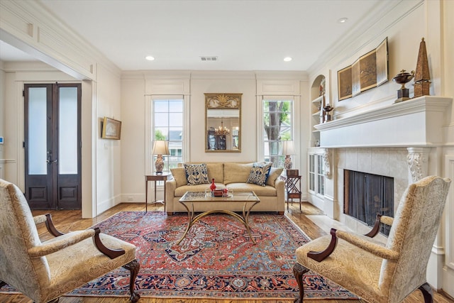 living area featuring a fireplace, built in shelves, wood finished floors, visible vents, and ornamental molding