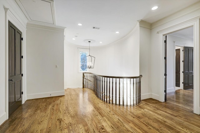 corridor with crown molding, wood finished floors, baseboards, a notable chandelier, and an upstairs landing