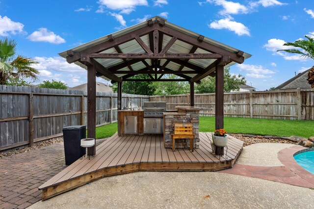 wooden terrace featuring grilling area, a lawn, exterior kitchen, a gazebo, and a fenced backyard