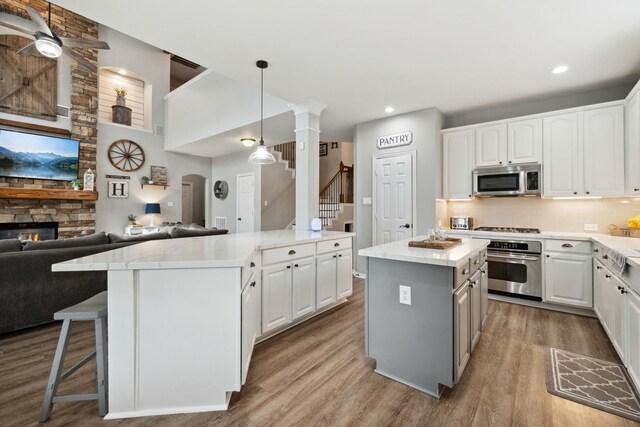 kitchen featuring white cabinets, appliances with stainless steel finishes, open floor plan, wood finished floors, and a kitchen island