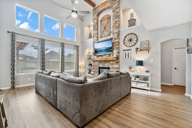 living area with a ceiling fan, arched walkways, a fireplace, baseboards, and a high ceiling