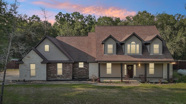 view of front of home featuring covered porch, a shingled roof, and a front lawn
