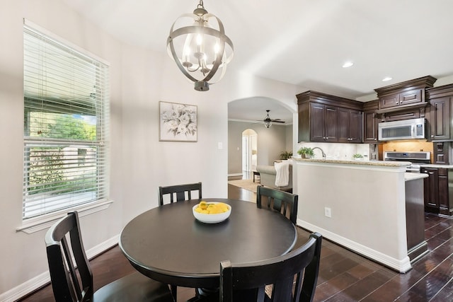 dining space with arched walkways, baseboards, ceiling fan with notable chandelier, dark wood-style floors, and recessed lighting
