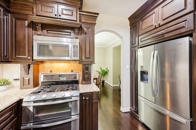 kitchen featuring dark wood-style flooring, appliances with stainless steel finishes, arched walkways, baseboards, and tasteful backsplash