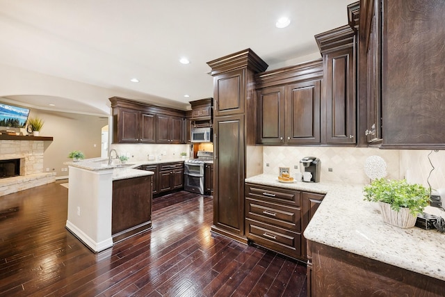 kitchen featuring a peninsula, dark brown cabinetry, dark wood finished floors, backsplash, and stainless steel appliances