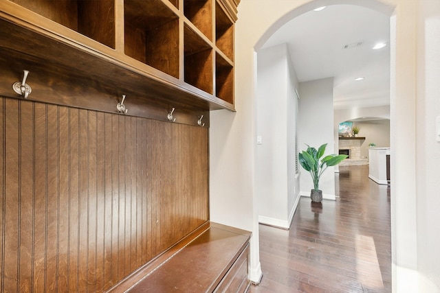 mudroom with arched walkways, a fireplace with raised hearth, hardwood / wood-style floors, and visible vents