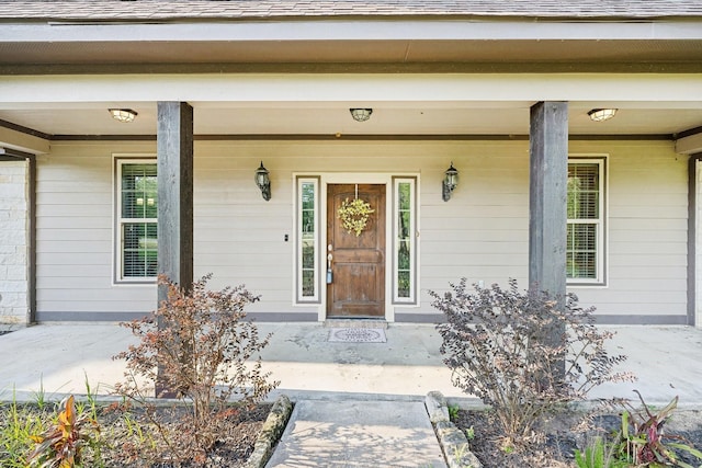 view of exterior entry with covered porch and a shingled roof