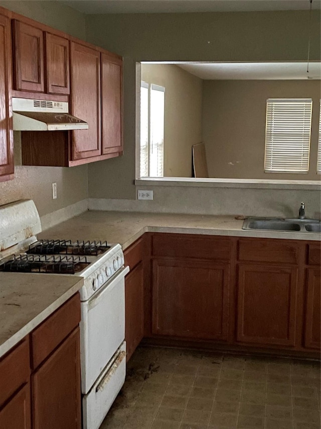 kitchen featuring brown cabinetry, a sink, light countertops, under cabinet range hood, and white range with gas stovetop